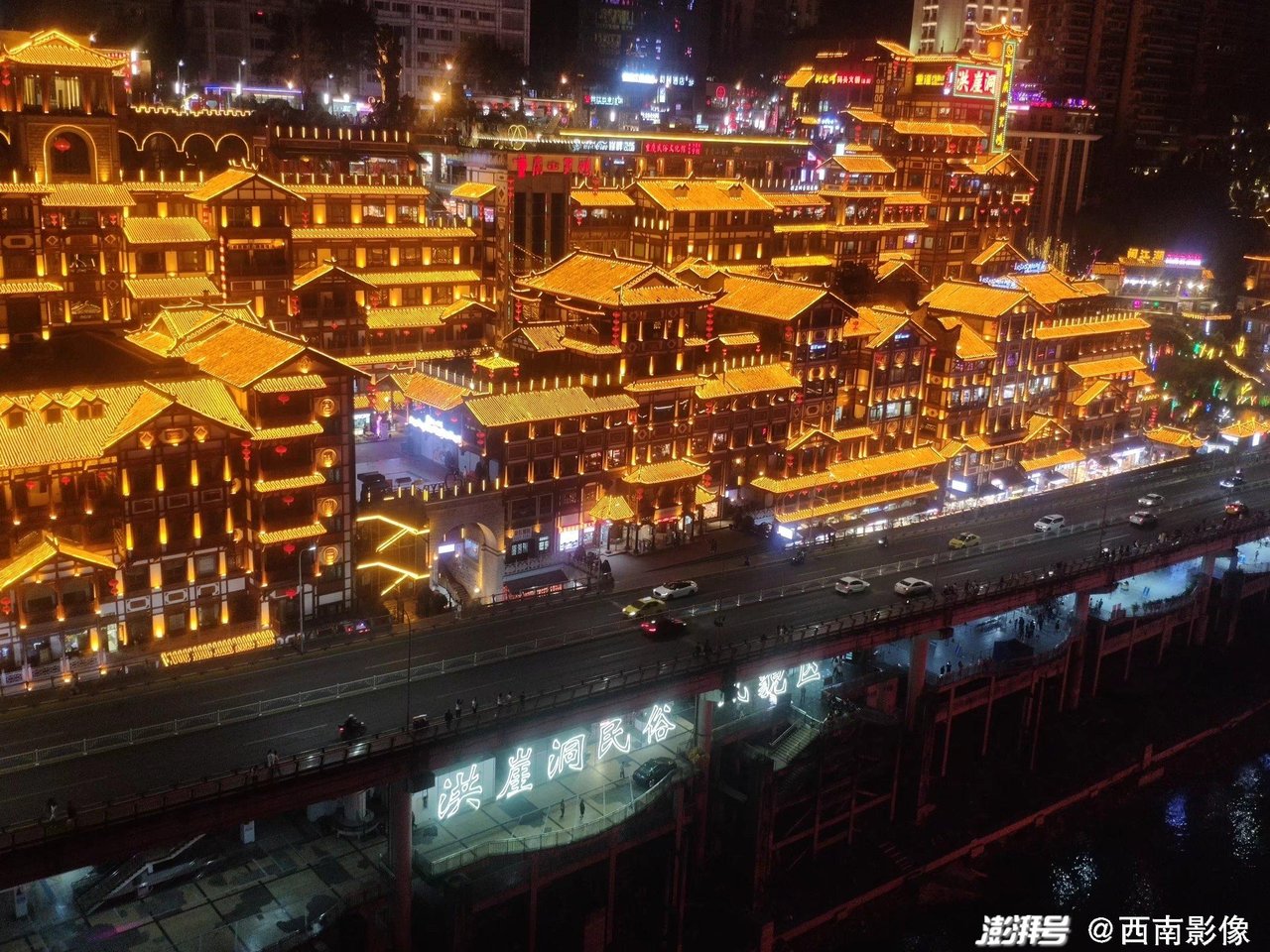 千厮门大桥与洪崖洞夜景，橙黄色灯光的吊脚楼群倒映在嘉陵江面上
