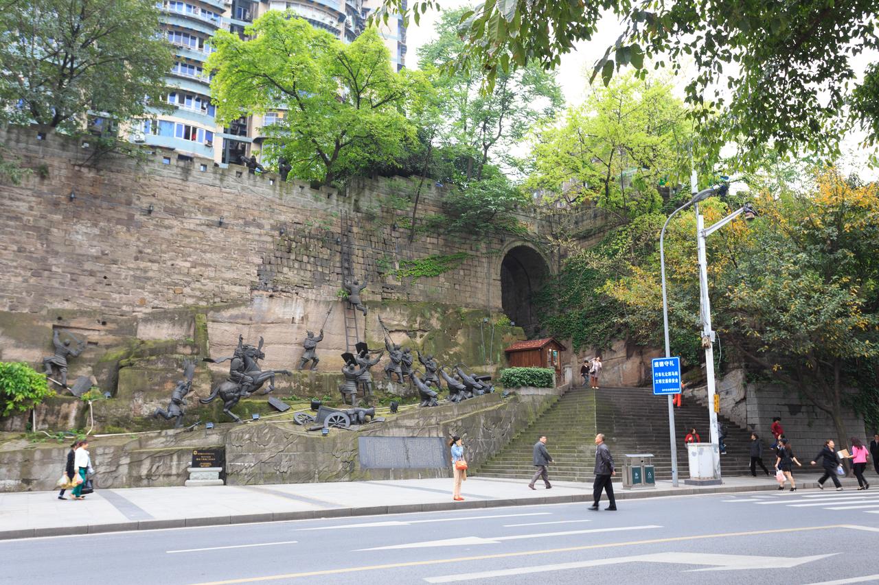 重庆通远门城门，石拱门上方是城楼和树林，门外有青铜雕塑