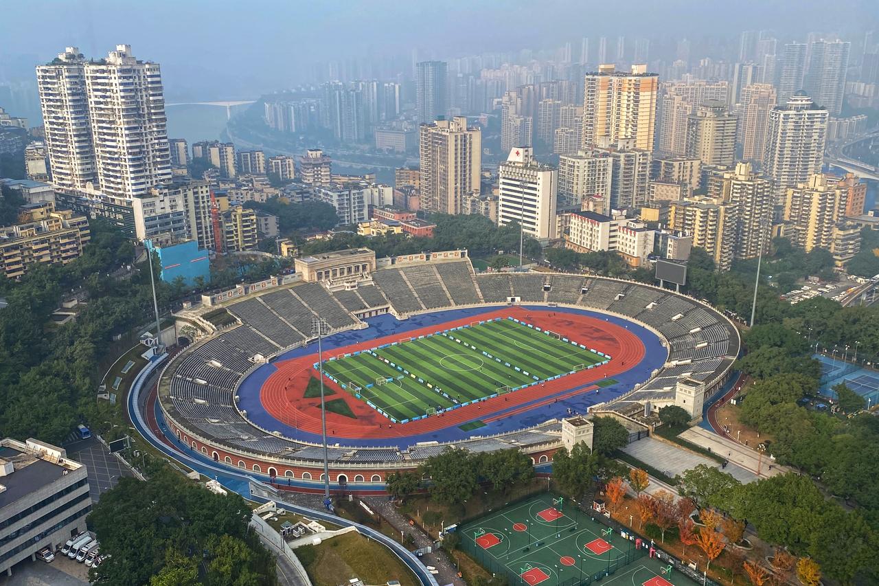 大田湾体育场全景，红色跑道环绕绿茵足球场，远处被建筑环绕