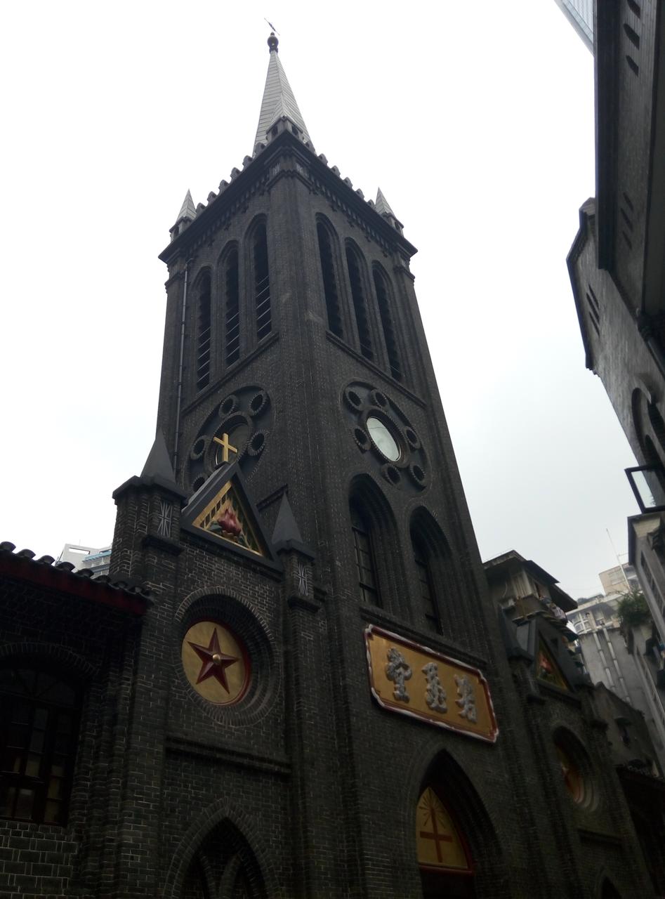 若瑟堂钟楼正面外观，青灰色砖石立面，山字形钟楼和红色十字架