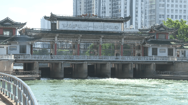A traditional Chinese-style building with a curved roof and decorative eaves spans over the water of
