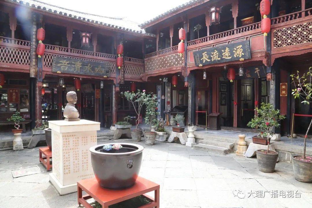 A traditional Chinese courtyard features wooden buildings with red lanterns, potted plants, statue s