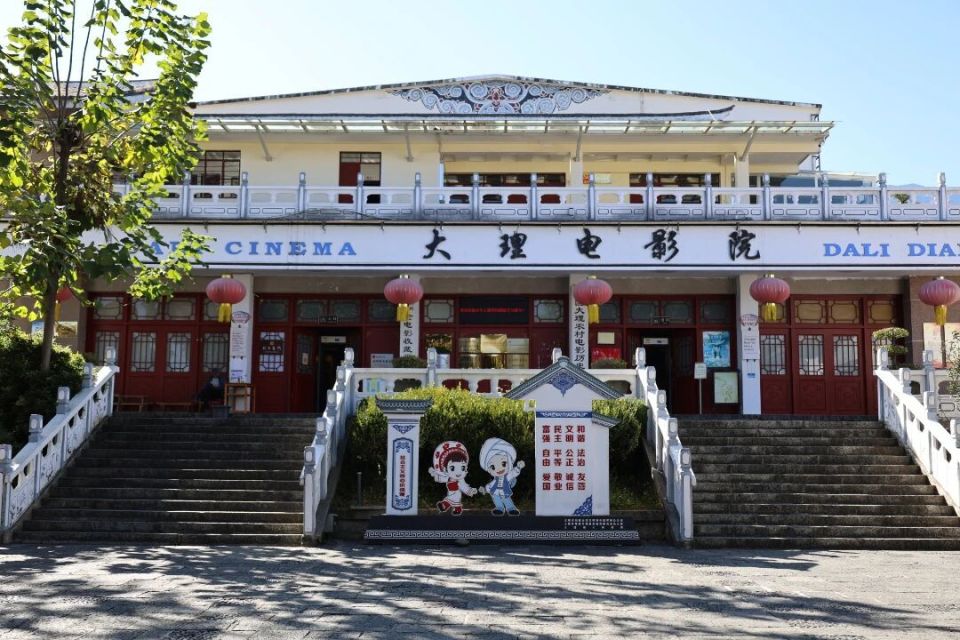 大理农村电影历史博物馆建筑外观：青瓦白墙的白族风格建筑，门头悬挂木质匾额，与周围旅游商品店形成视觉反差
