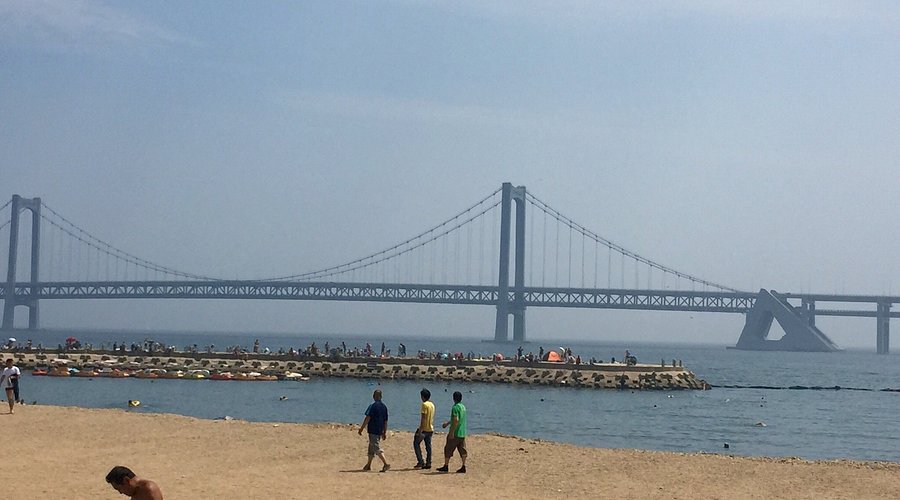 Three people walk along the sandy shore of Dalian Xinghai Park's water bathing a