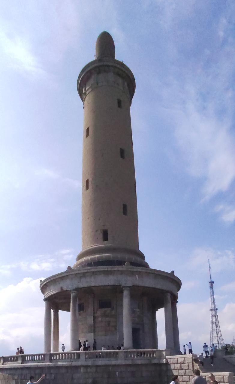 A white marble tower with a rounded base and a narrow, tall structure rises agai