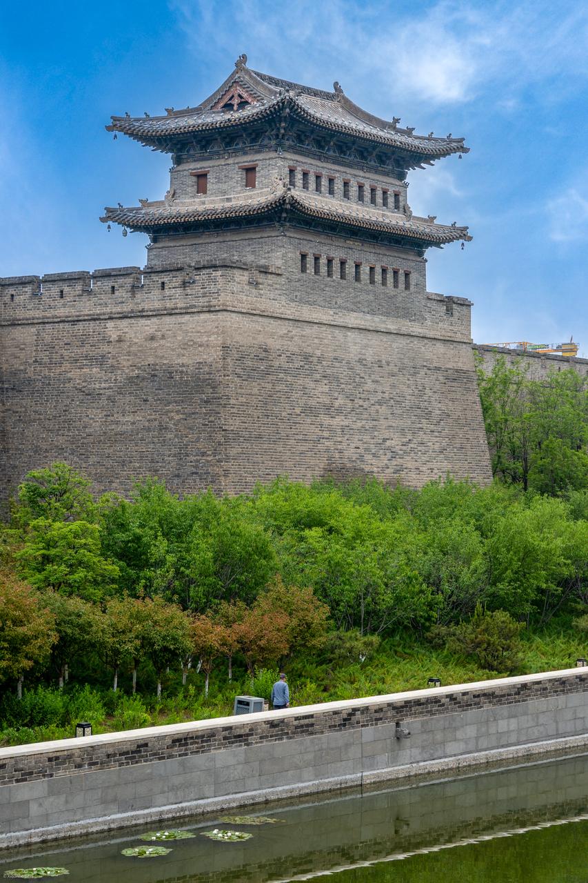 城墙脚下护城河与带状公园，水面种植睡莲，远处现代建筑可见