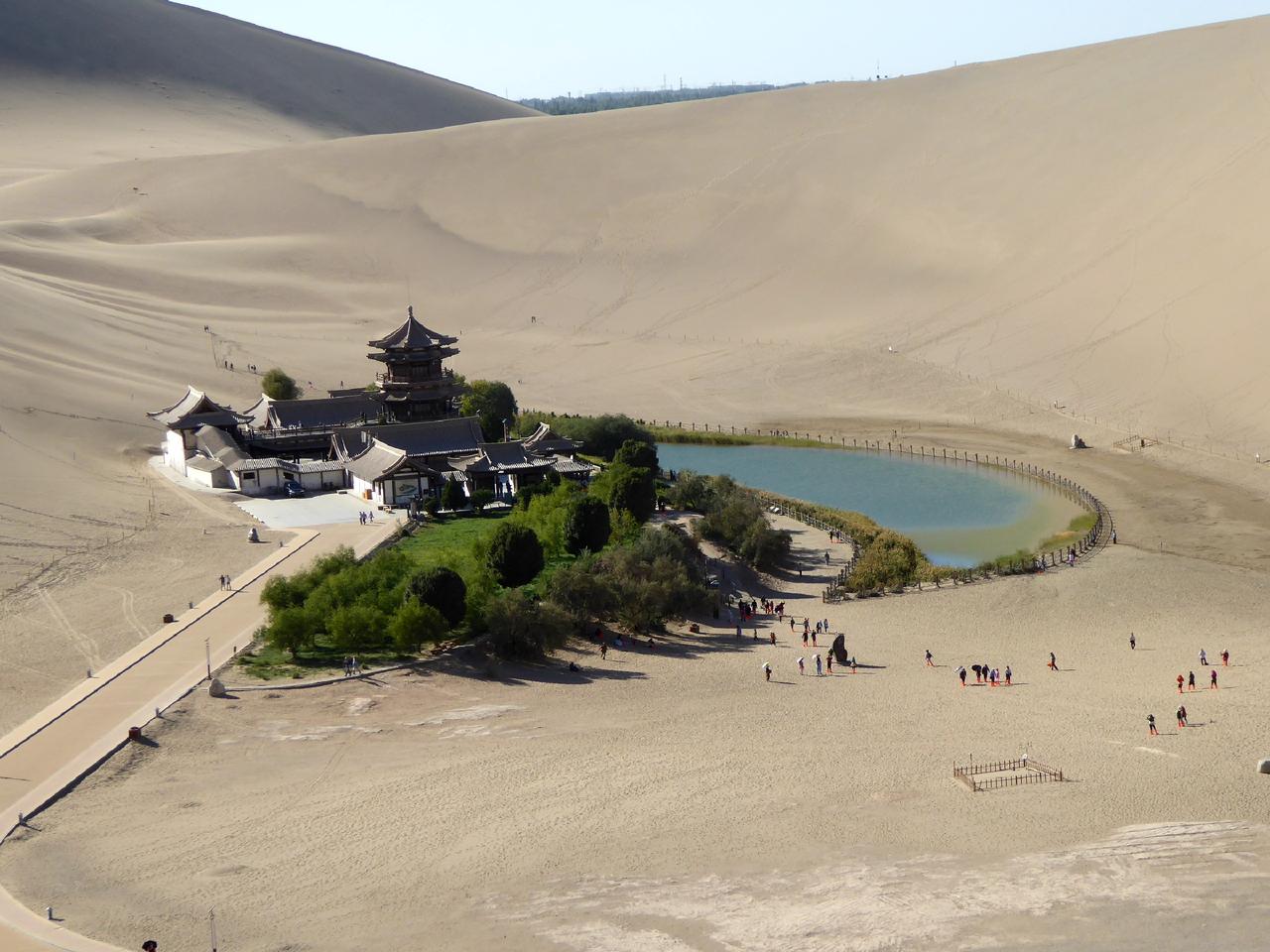 从鸣沙山沙丘顶北望：前景沙丘、中景月牙泉、远景绿洲边界和敦煌市区天际线