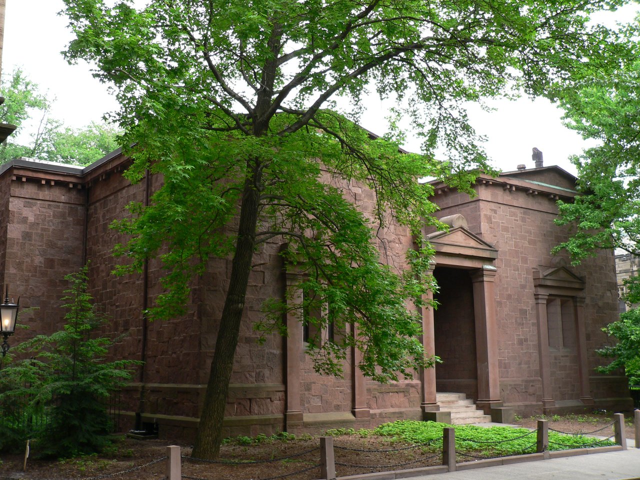 Contemporary angled view of the Skull and Bones building, with its brownstone blocks, formal entrance, blind bays, trees, and low service openings
