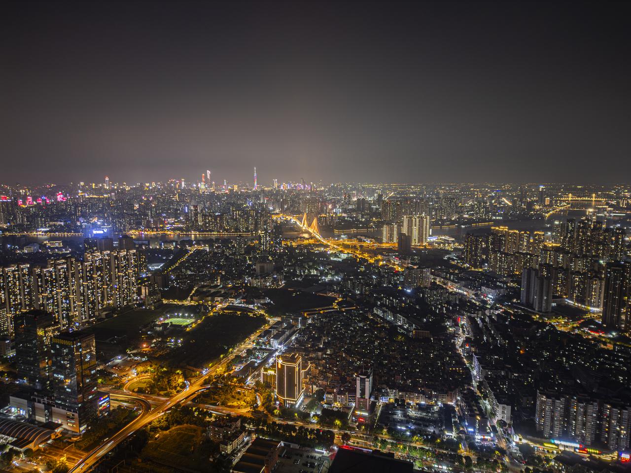 The image shows a vibrant, illuminated cityscape at night with numerous high-rise buildings, bright lights along the riv