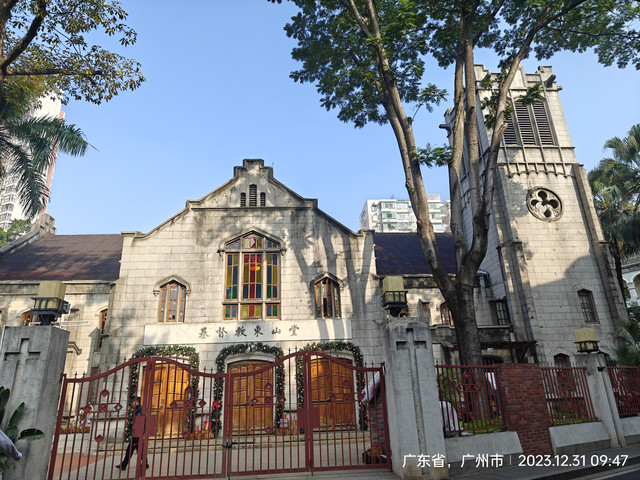 A historic church with a Gothic architectural style features colorful stained glass windows, surrounded by a red metal f