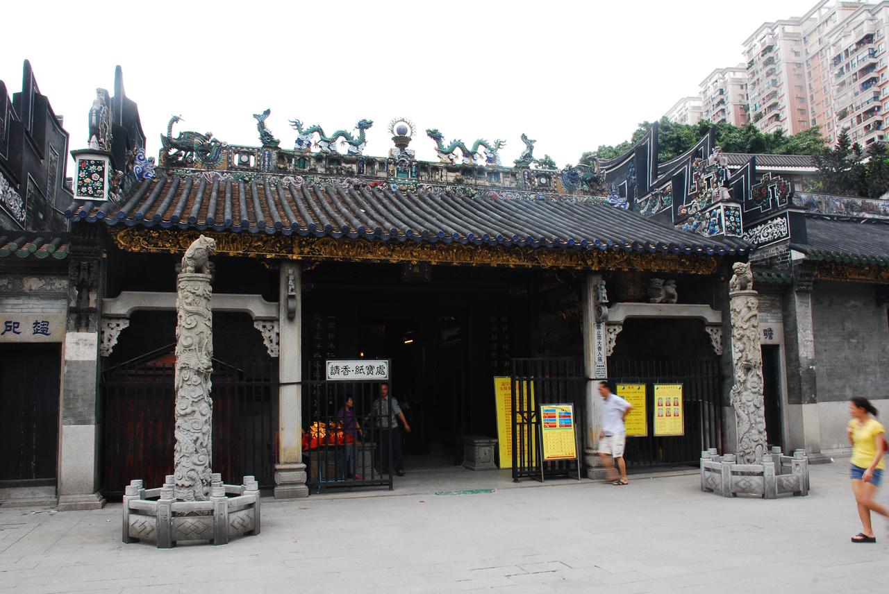 A group of people is gathered in front of a traditional Chinese temple decorated with dragons and intricate carvings, wi