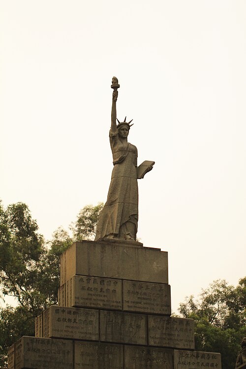 A replica of the Statue of Liberty stands atop a monument inscribed with Chinese characters, located near a traditional 
