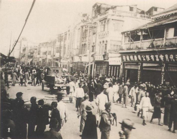 A bustling street scene in Guangzhou showing people and vehicles, with the Zhonglou (Bell Tower) and the four-term trans