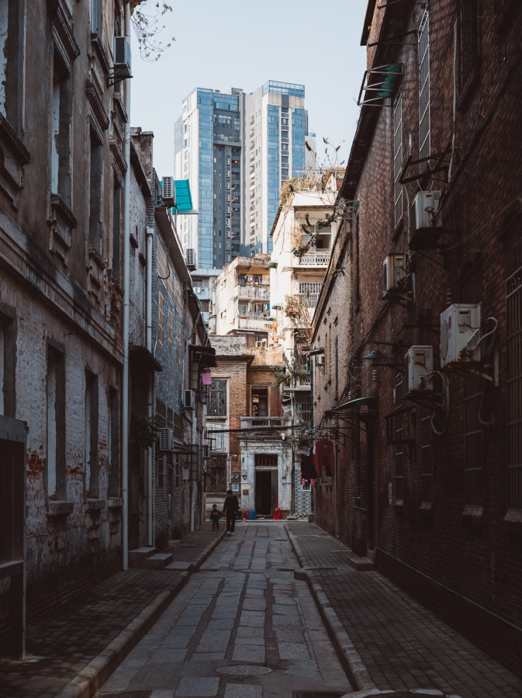 A narrow alleyway in Guangzhou featuring old and weathered residential buildings, with laundry hanging outside, air cond