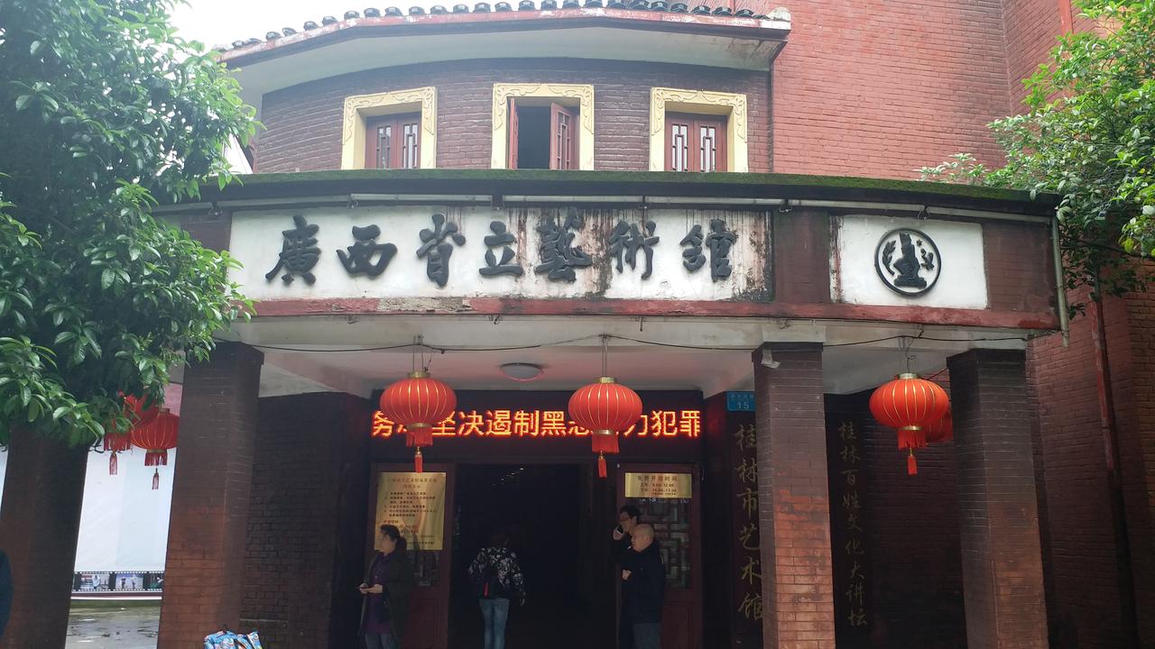广西省立艺术馆红墙青瓦的正立面外观，凸字形平面上三件人物浮雕清晰可见