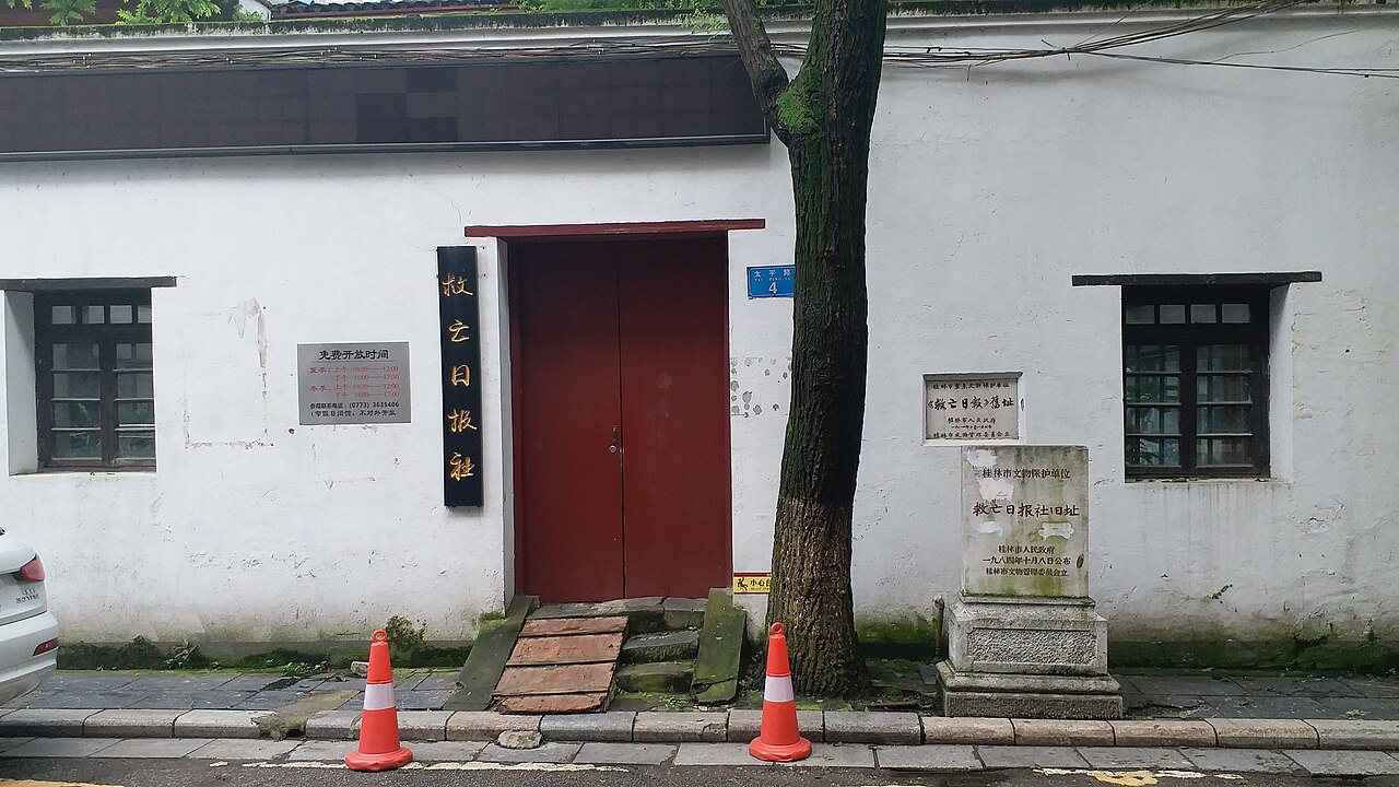 救亡日报社旧址建筑外景，白墙红门的两层砖木小楼，门前石碑刻着旧址身份