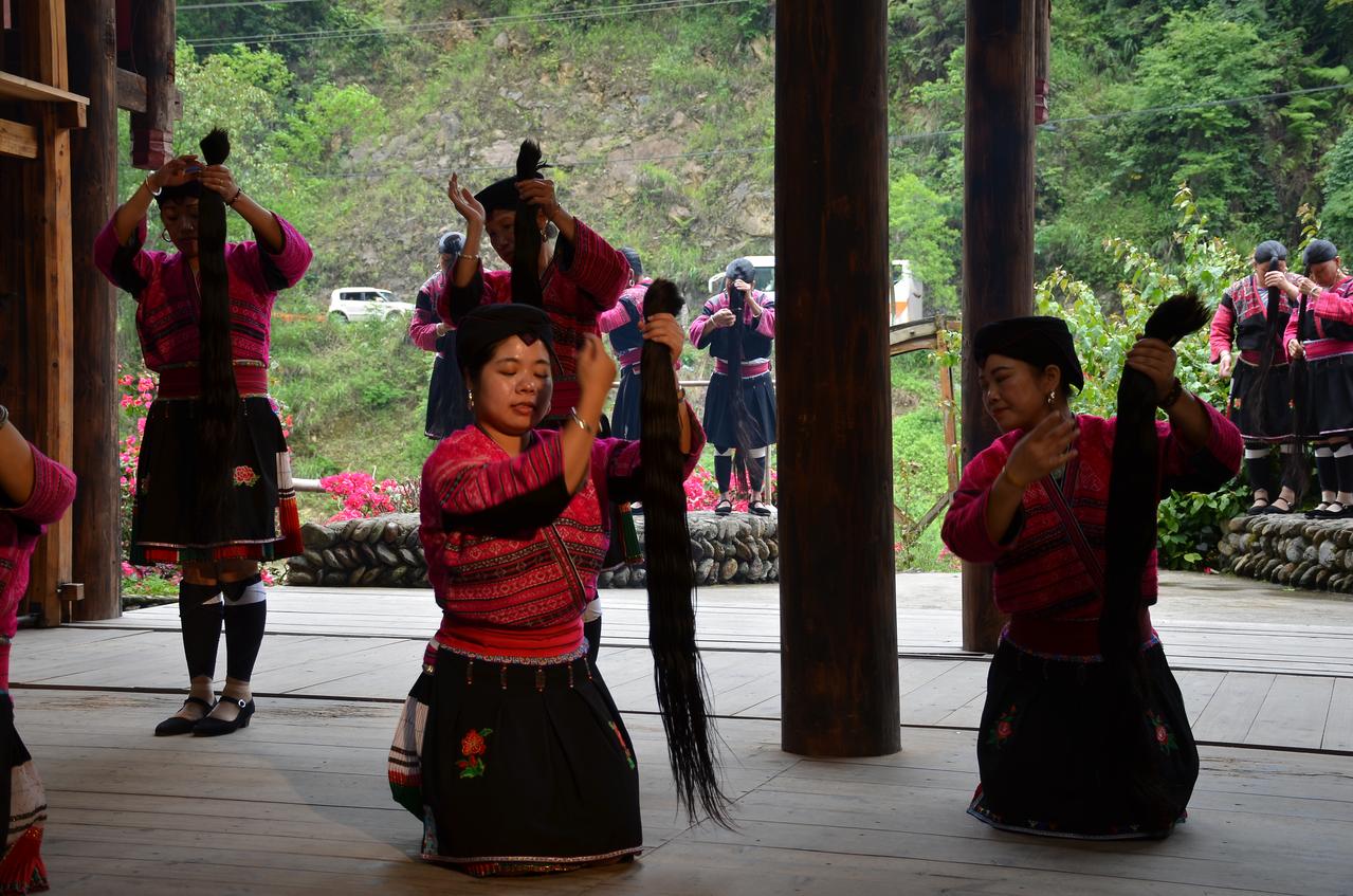 红瑶女性在表演场上展示长发舞蹈，红色传统服饰在绿色山野中格外醒目