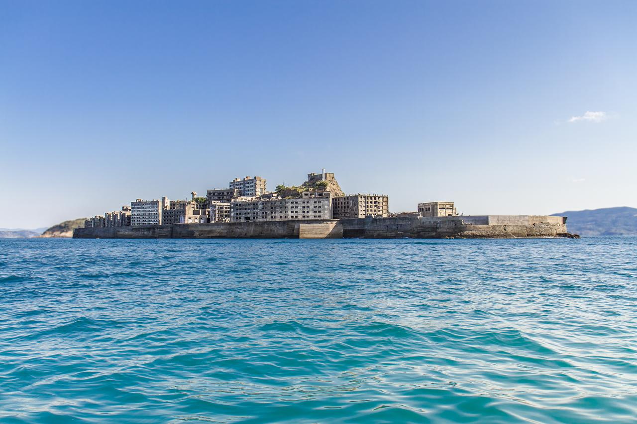 从海上看到的军舰岛全貌，灰色混凝土建筑群密集排列，防波堤垂直从海面升起