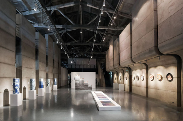 真如堂老厂房改造展厅内部，保留厂房钢桁架屋顶，标准化展柜陈列陶瓷茶器、花器和香具
