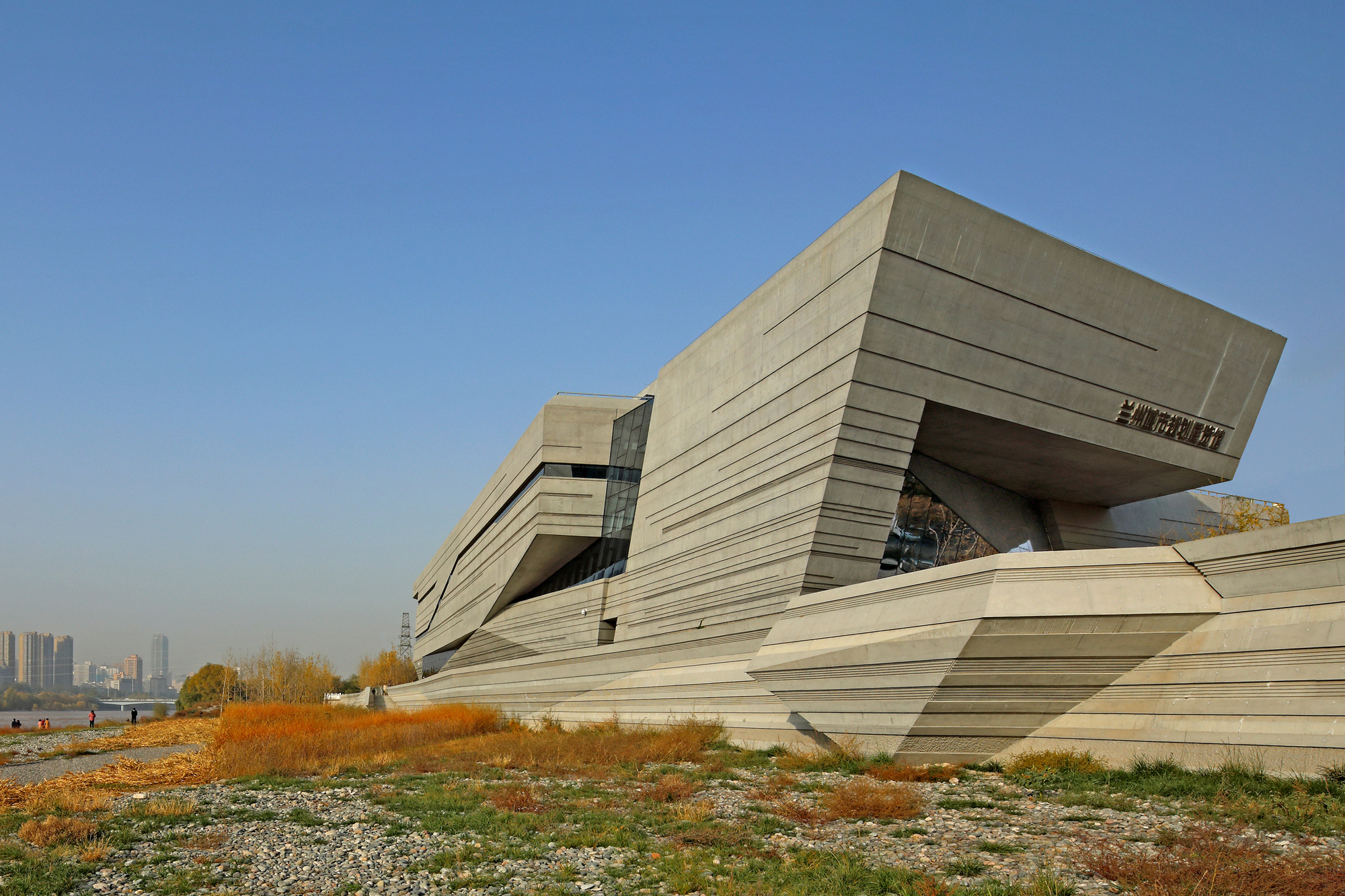 A modern, angular building with a concrete facade and prominent overhangs, set a