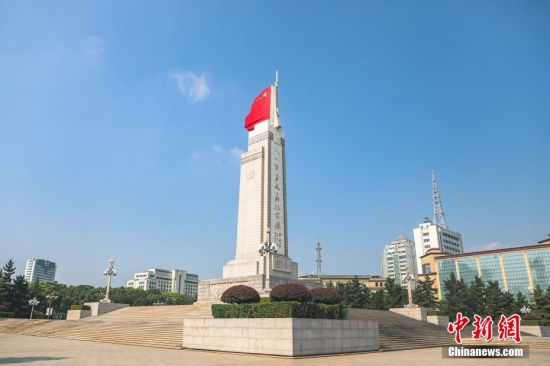 八一南昌起义纪念塔远景，塔身在蓝天与城市建筑背景下矗立