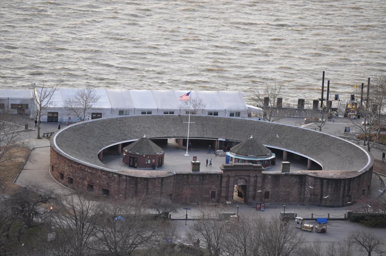 Castle Clinton 正面远景，可见圆形红砂岩外墙和公园草坪