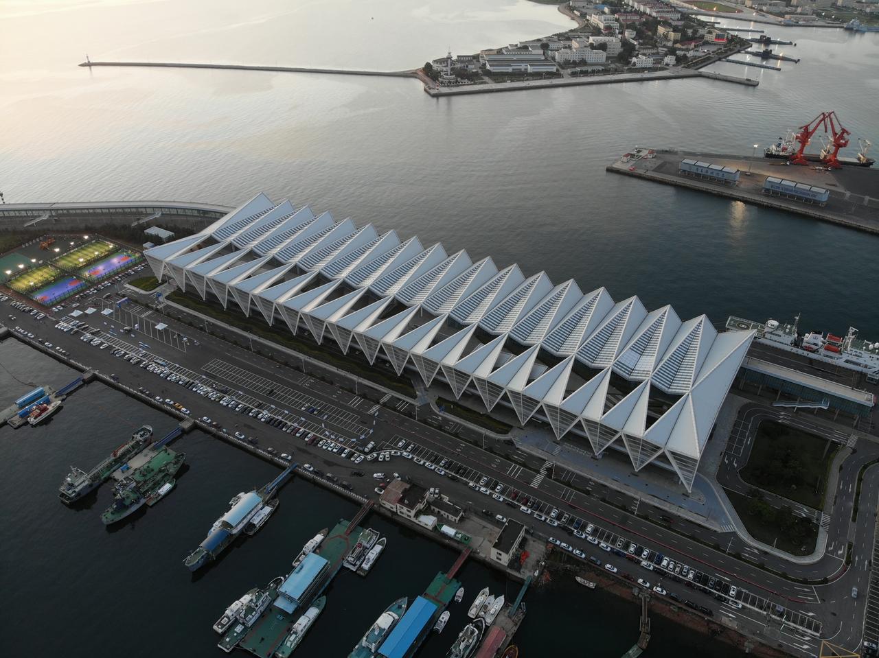 邮轮母港客运中心外观，白色折线形屋顶和暴露的钢结构骨架向海面延伸