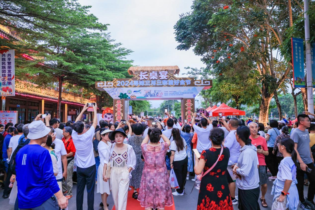 保亭三月三长桌宴，矮桌上摆满黎族特色食物，游人在两侧就座用餐