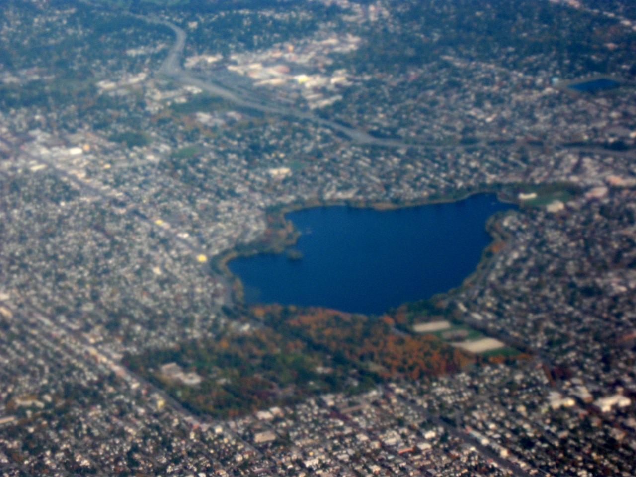 从空中向东北看 Green Lake 与周围密集街区，湖体居中，南端 Aurora Avenue/I-5 高速从后方穿过