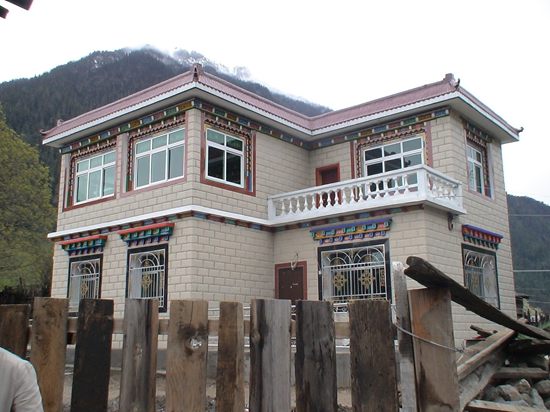 一栋新建藏式民居近景，可见藏式彩绘窗框与砖混结构墙体的结合