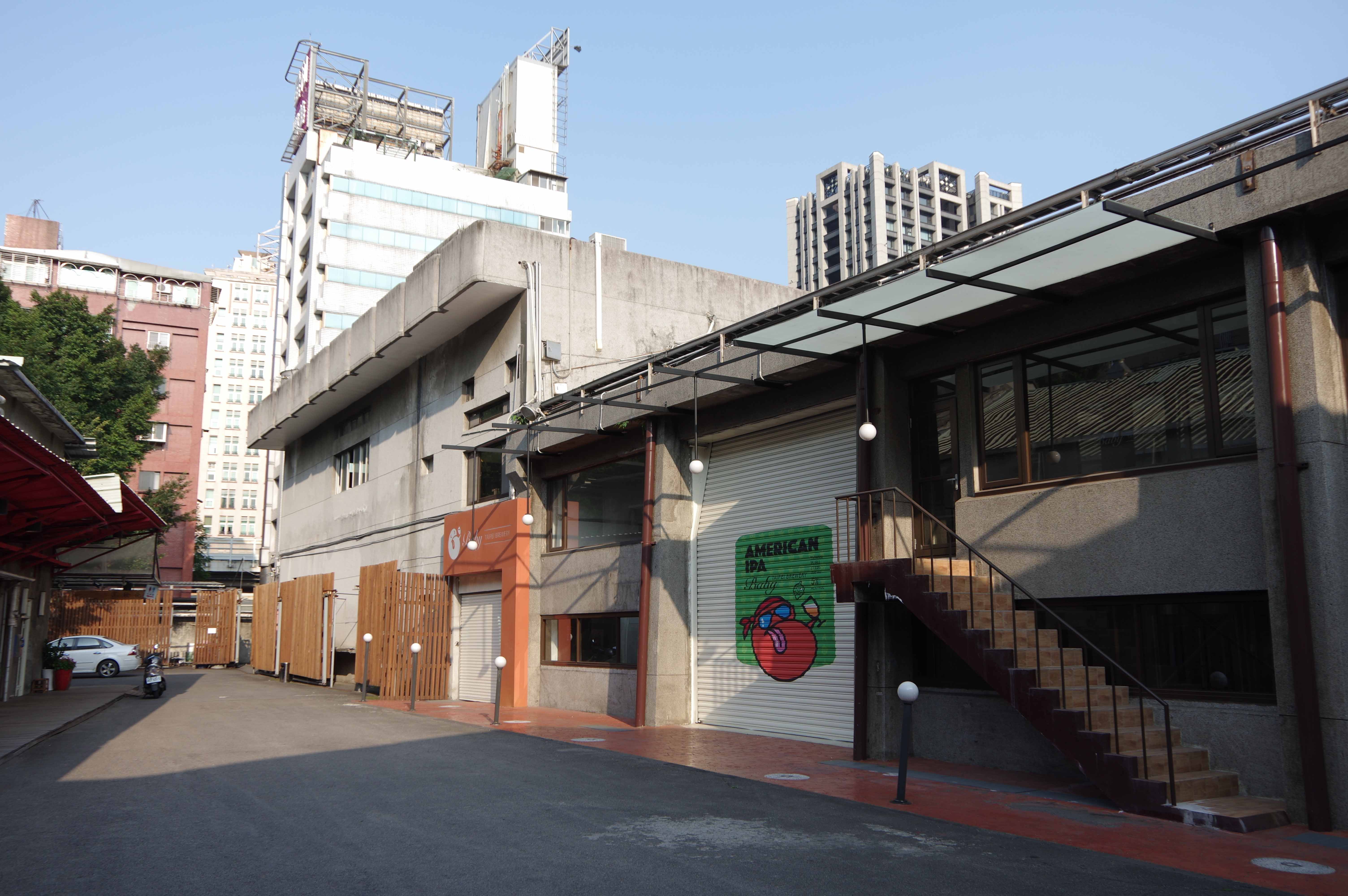 一座具有紅磚外牆的工廠建築，配有煙囪和金屬結構的設備，周圍有綠樹與植物，天空晴朗。