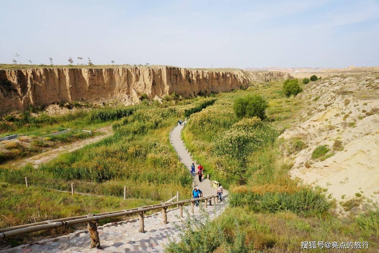 A winding pathway through a lush green valley with ancient rammed earth walls an