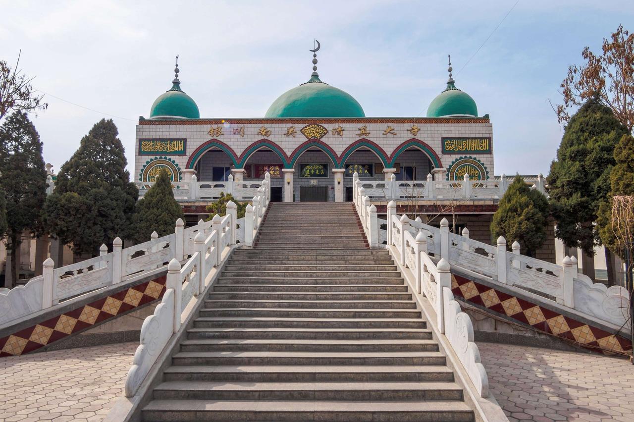 三座歇山顶的清真寺建筑在树木之间，前有一段阶梯通向门口，门楼装饰有阿拉伯文字和图案。