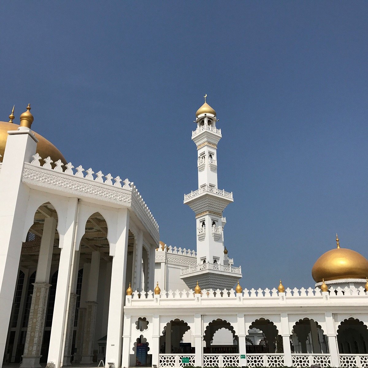 A white mosque with golden domes and a tall minaret stands against a clear blue 